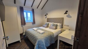 Une chambre à coucher avec un lit, des tables de chevet, une fenêtre avec des rideaux et un radiateur.