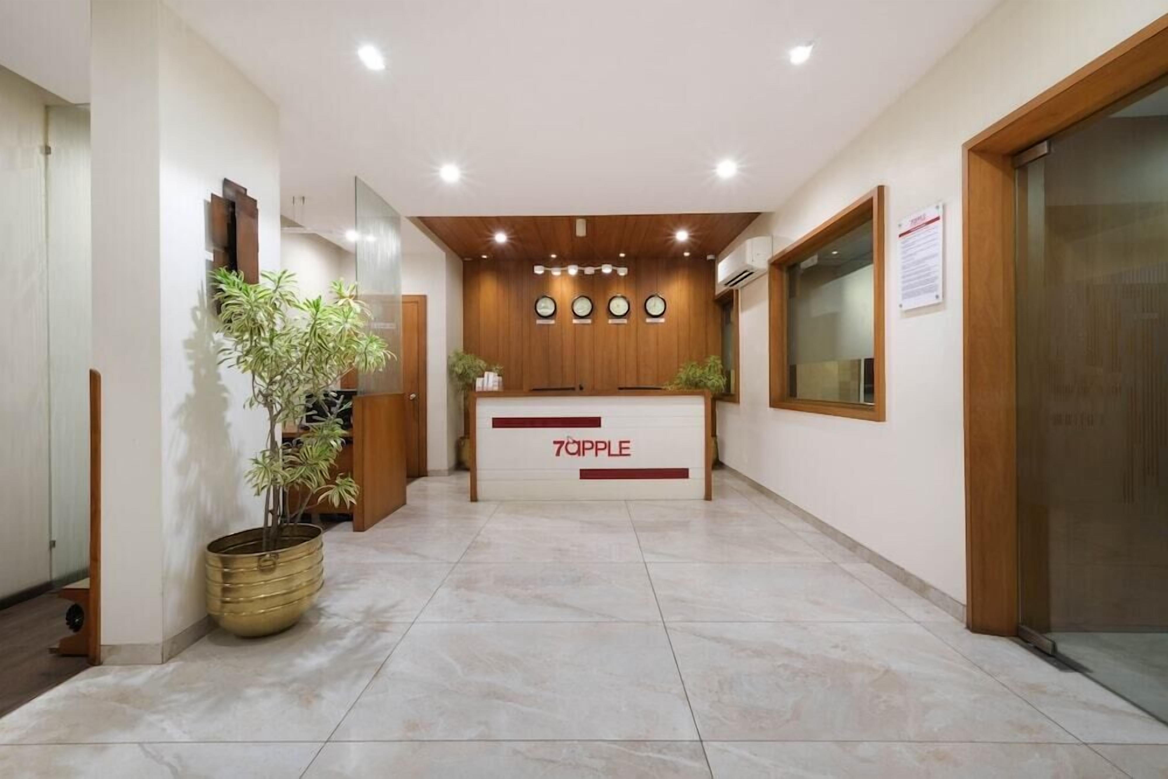 A reception area with a wooden reception desk labeled "7APPLE," a potted plant, and a wall-mounted clock.