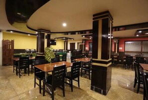 Un restaurant doté de nombreuses tables et chaises, d’une colonne centrale et d’un sol carrelé.