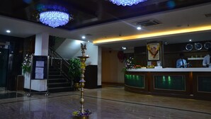 A lobby with a reception desk, a staircase, chandeliers, and a decorative pillar. - MG Hotel Udayee International (Tirupati)