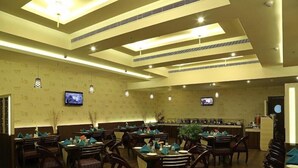 A restaurant with wooden tables and chairs, ceiling lights, and two televisions on the walls. - Keys Hotel Vihas (Tirupati)