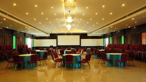 A conference room with round tables, red chairs, a large screen, and a chandelier. - Keys Hotel Vihas (Tirupati)