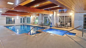 A large indoor swimming pool with two separate sections, wooden beams on the ceiling, and a seating area with tables and chairs.
