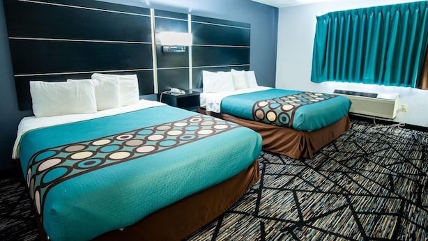 Habitación de hotel con dos camas, un cabecero grande, una ventana con cortinas y una alfombra estampada.