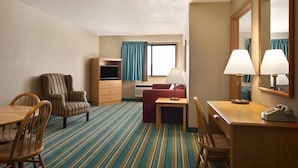 Habitación de hotel con alfombra a rayas, un escritorio de madera, una silla, un sofá, un televisor y un espejo.