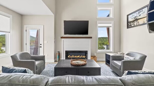 Een moderne woonkamer met een open haard, een flatscreen televisie erboven en een groot raam met een prachtig uitzicht.
