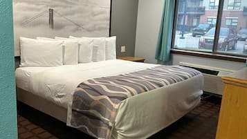 Une chambre d’hôtel avec un lit, une fenêtre donnant sur des immeubles, un mur orné d’un tableau et un luminaire au plafond.
