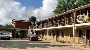Ein Motel mit zweistöckiger Bauweise, einem überdachten Parkbereich und einem roten Auto vor der Fassade.