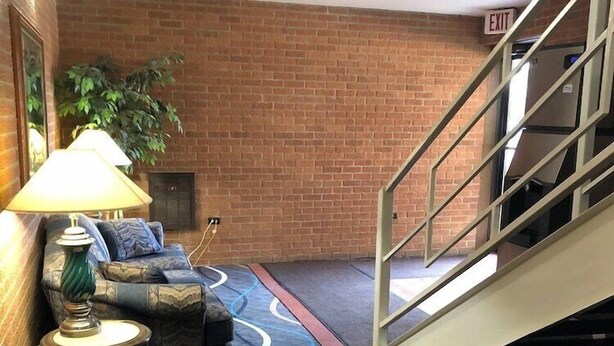 Eine Hotellobby mit Backsteinwand, einer Treppe, einer Couch mit Kissen, einer Lampe und einem Teppich mit Wellenmuster.