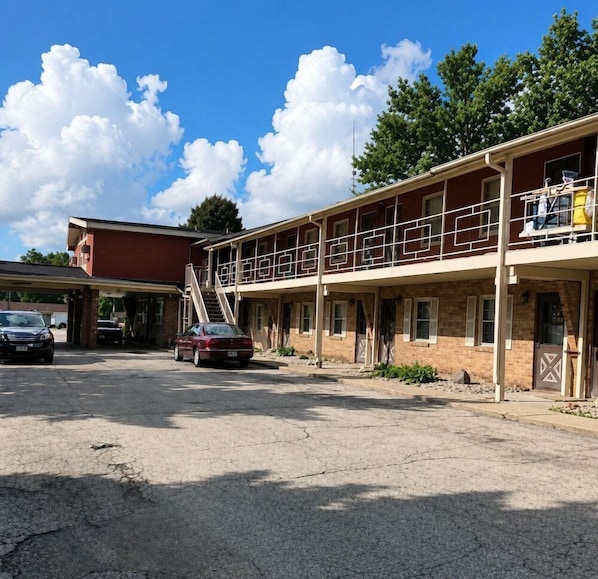 A motel with a two-story structure, a parking lot, and a red building in the background. - Mcgoverns Hotel and Suites (Sun Prairie)
