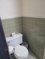 Un baño pequeño y funcional con inodoro, un bote de basura y un dispensador de papel higiénico.