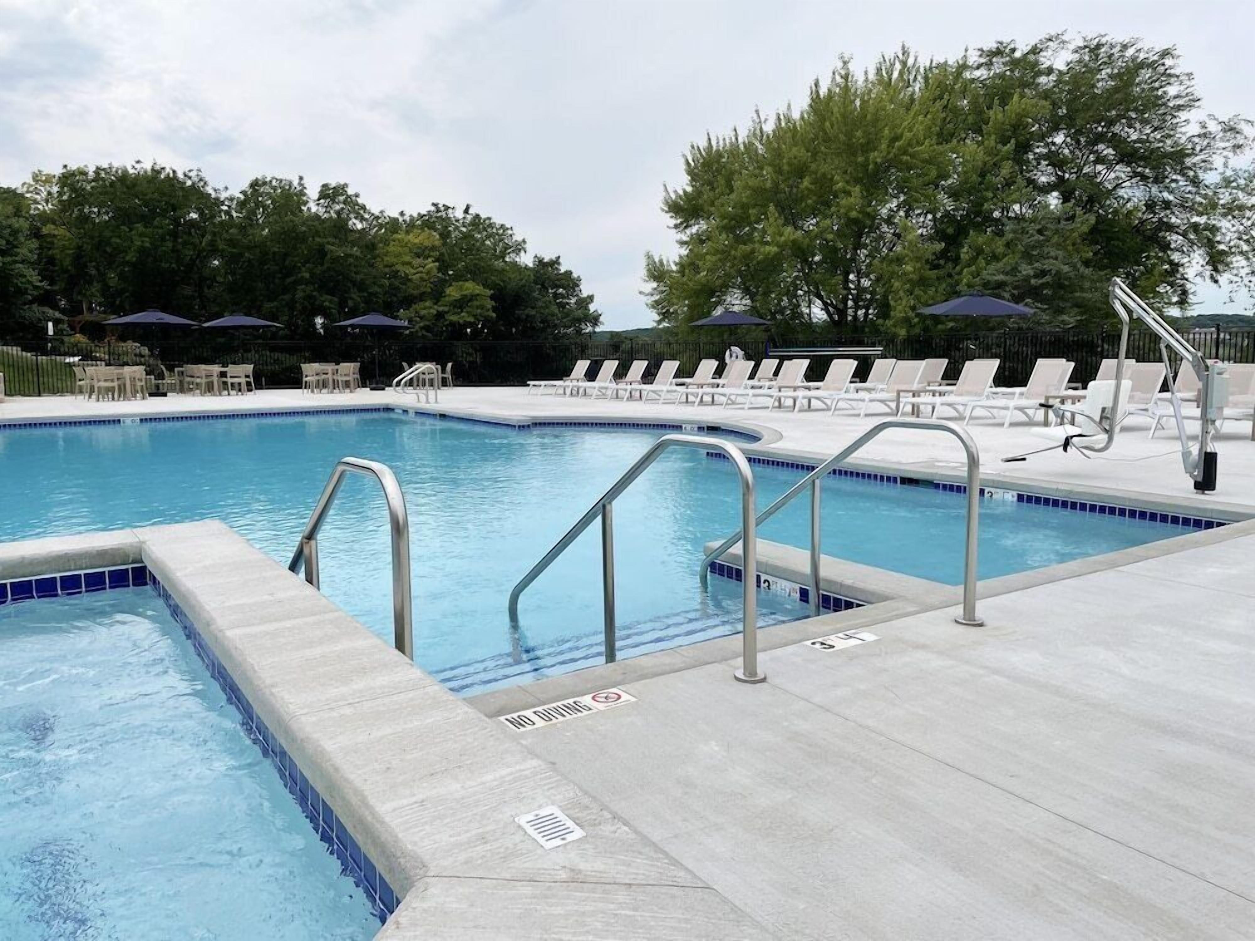 Una piscina con borde de azulejos, un cartel de prohibido bucear y sillas de descanso alrededor.