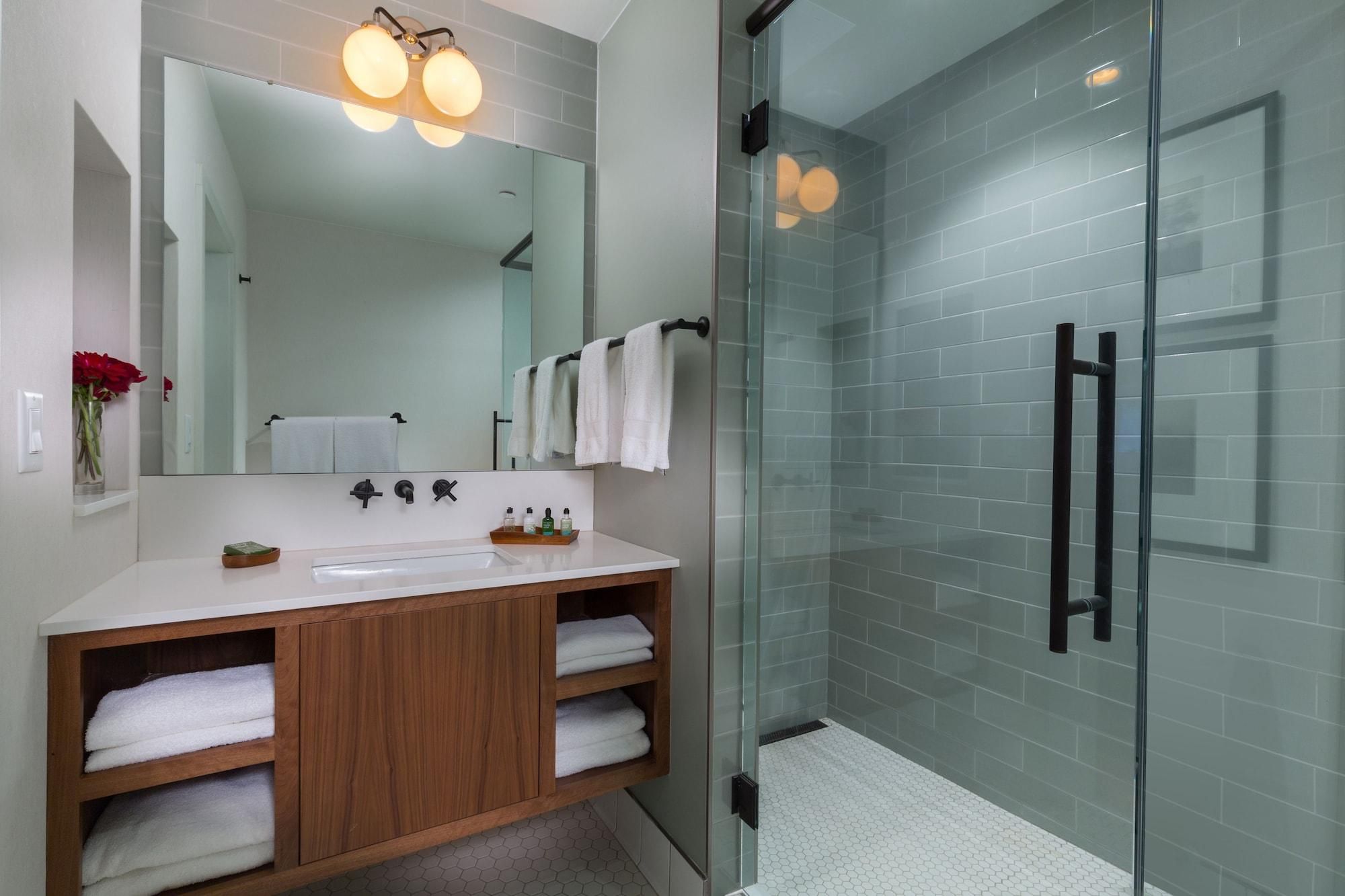 A modern bathroom with a glass shower enclosure, a large mirror, and a wooden vanity with two sinks.