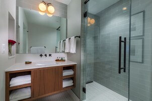 Un baño moderno con cabina de ducha de vidrio, un espejo grande y un mueble de tocador de madera con dos lavamanos.