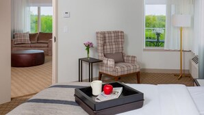 A hotel room with a bed, a chair, a small table with a tray, a window with a view, and a door leading to another room. - The Ingleside Hotel (Pewaukee)