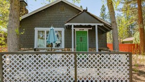 Una pequeña cabaña de madera con puerta verde, un porche blanco y un cerramiento de celosía.
