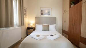 Une chambre bien rangée, avec un lit, une table de chevet, une commode, une tête de lit, une armoire et une fenêtre avec des rideaux.