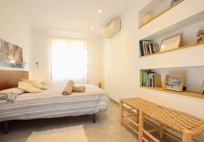 Une chambre à coucher avec un lit, un banc, une bibliothèque et une fenêtre avec des rideaux.
