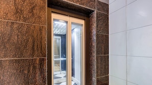 Een moderne lift met glazen deuren, een marmeren wand en een betegelde vloer.