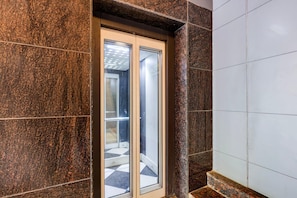 A modern elevator with glass doors, surrounded by dark granite walls and white tiled floors.