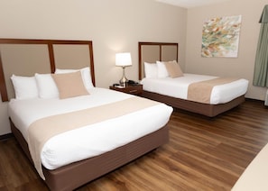 A hotel room with two beds, wooden headboards, a nightstand with a lamp, and a painting on the wall. - D. Hotel and Suites (Holyoke)