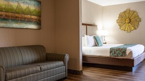 A hotel room with a sofa, a bed, a painting, and a decorative wall piece. - D. Hotel and Suites (Holyoke)