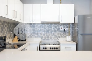 A modern kitchen with white cabinets, a stainless steel stove, and a built-in oven. - Bloomfields Premium 2BR in Parkside (Abu Dhabi)
