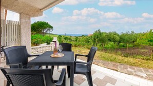 Eine Terrasse mit Tisch und Stühlen, einer Flasche und einem Glas, mit Blick auf einen Weinberg und eine weite Landschaft.