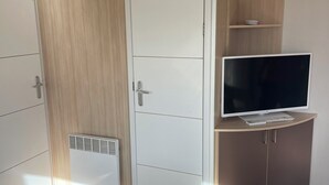 Ein Zimmer mit Kleiderschrank, Fernseher auf einer Kommode und Lüftungsgitter an der Wand.