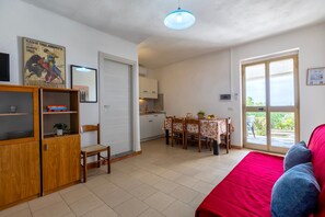 A compact living space with a kitchenette, a dining area with a table and chairs, a red sofa, and a large window.