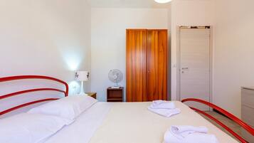 Une chambre d’hôtel avec un lit, une armoire en bois, une porte blanche, un ventilateur et une table de chevet avec une lampe.