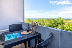 Ein Balkon mit Tisch für zwei Personen, mit Blick auf das Meer und viel Grün.
