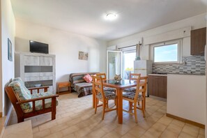 A compact living space with a sofa, dining table, chairs, a TV, a kitchen area, and a window. - Apartment 'Con Balcone' with Sea View, Wi-Fi and Air Conditioning (La Muddizza)