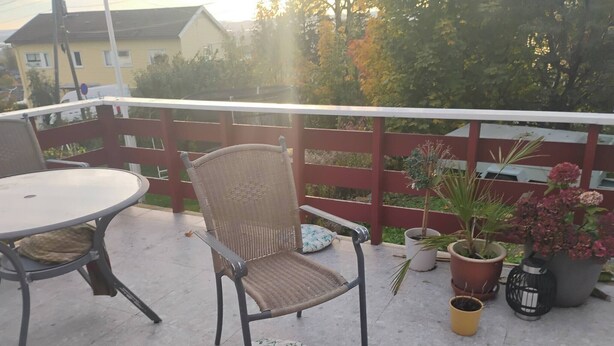A balcony with a wicker chair, a round table, and potted plants. - Room-a Nice Room in a House (Oslo)