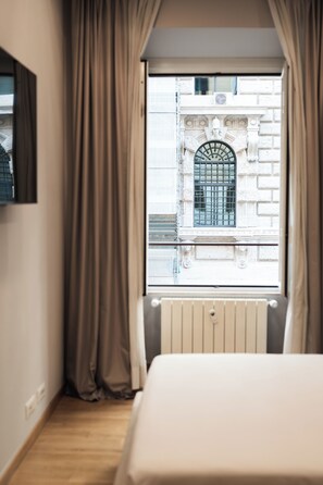 Une chambre d’hôtel avec une grande fenêtre, des rideaux, un radiateur et un lit.
