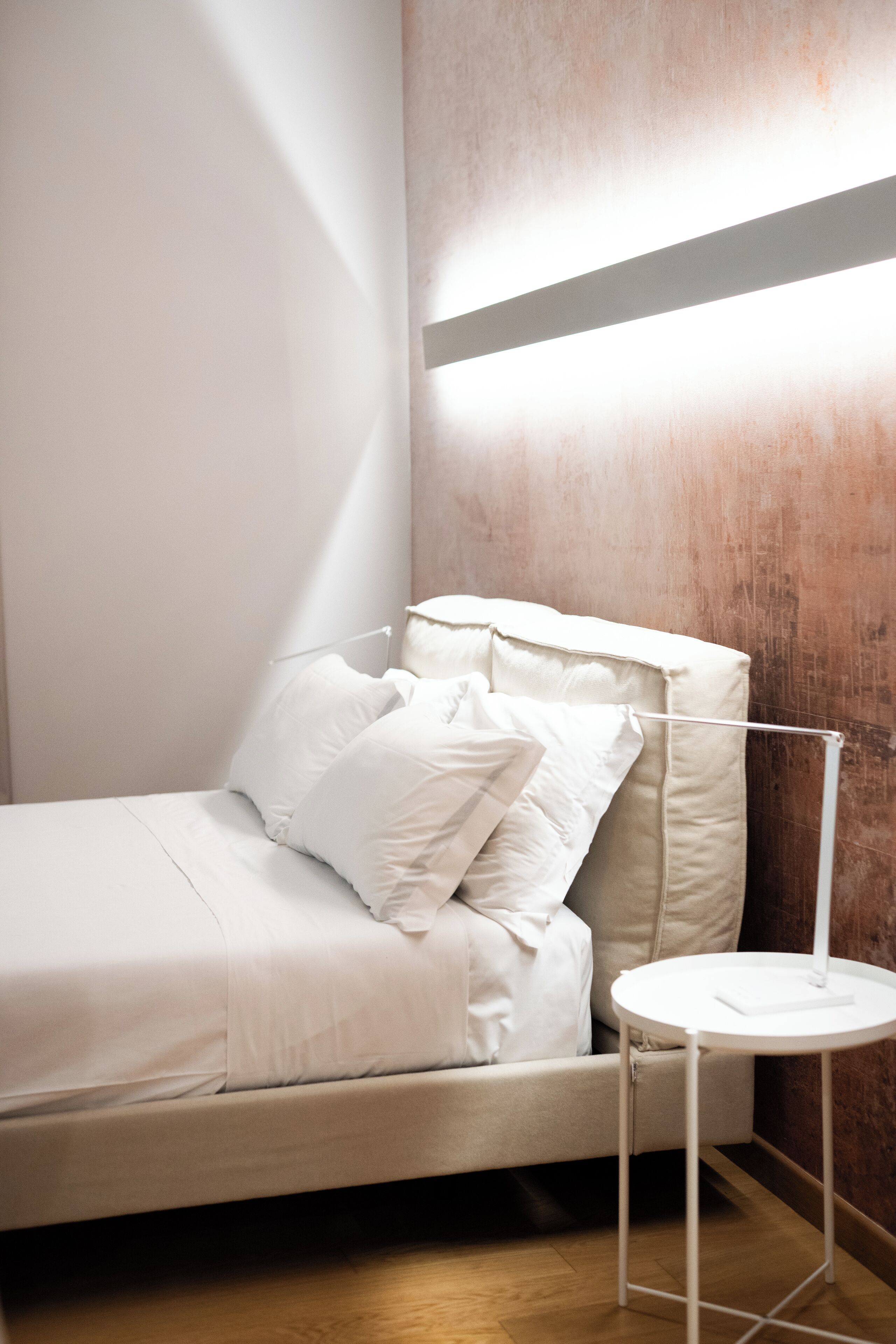 A modern bedroom with a bed, pillows, a bedside table, and a wall-mounted light fixture.