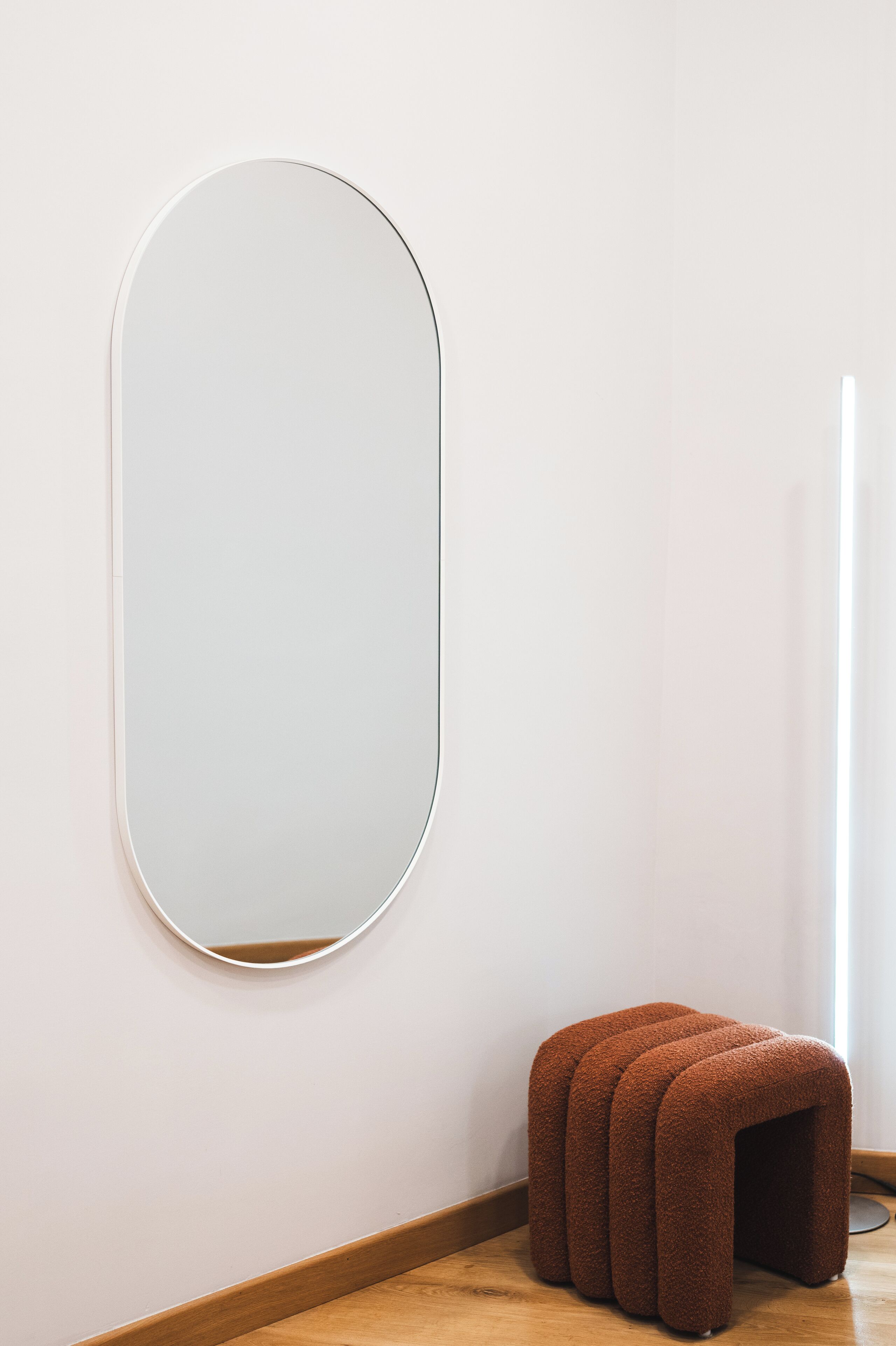 A minimalist room with a large mirror on the wall and a brown stool.