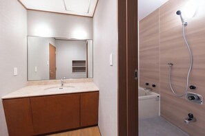 A bathroom with a wooden vanity, a mirror, a shower with a handheld showerhead, and a toilet. - Kusatsu Onsen Hotel Resort (Kusatsu)