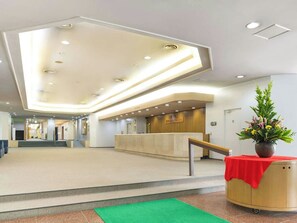 Un hall d’entrée spacieux avec un comptoir de réception, une moquette verte et une plante en pot.