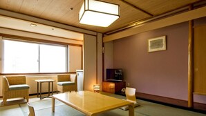A traditional Japanese room with tatami flooring, a low table, two cushioned chairs, a television, and a sliding door. - Kusatsu Onsen Hotel Resort (Kusatsu)