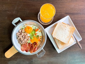 A breakfast plate with eggs, sausage, and toast, and a glass of orange juice on a wooden table. - Ban Nai Amphoe (Nakhon Ratchasima)
