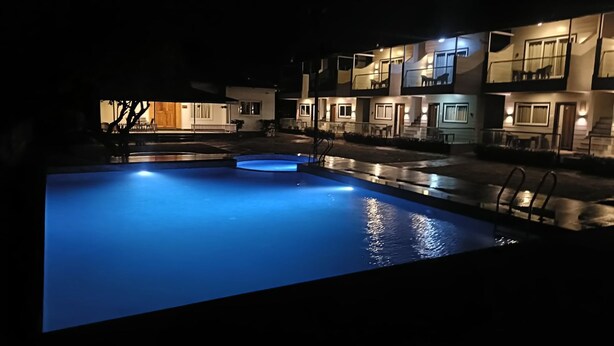 A swimming pool with a blue light at night, surrounded by a building with multiple balconies and windows. - Maooli Home Stay (Mahabaleshwar)