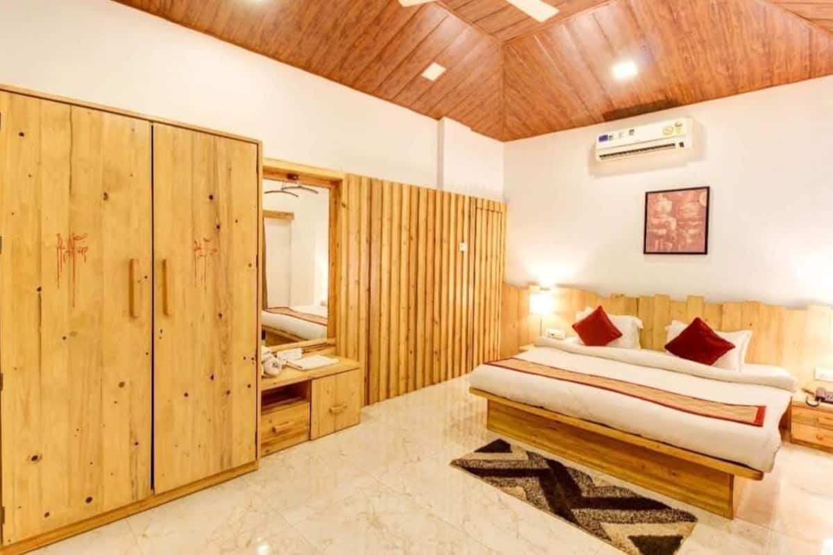 A bedroom with a large wooden wardrobe, a bed with red pillows, and an air conditioning unit on the wall.