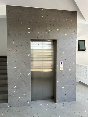 An elevator with a speckled gray wall, a blue accessibility sign, and a small window on the right. - 2bedroom beachfront Apartmnt Mombasa,Seaview,Ac,pool,gym,restaurant,beach access (Mombasa)