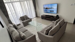 A modern living room with a sofa set, a glass coffee table, and a flat-screen TV mounted on the wall. - 2bedroom beachfront Apartmnt Mombasa,Seaview,Ac,pool,gym,restaurant,beach access (Mombasa)
