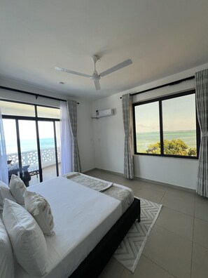 A bedroom with a large bed, a ceiling fan, an air conditioning unit, and a view of the sea. - 2bedroom beachfront Apartmnt Mombasa,Seaview,Ac,pool,gym,restaurant,beach access (Mombasa)