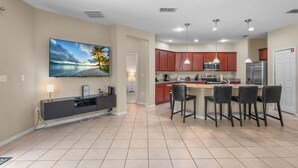 A modern kitchen with a dining area, a flat-screen TV, and a large painting on the wall. - 4 Bed Close to Disney Private Pool (Kissimmee)