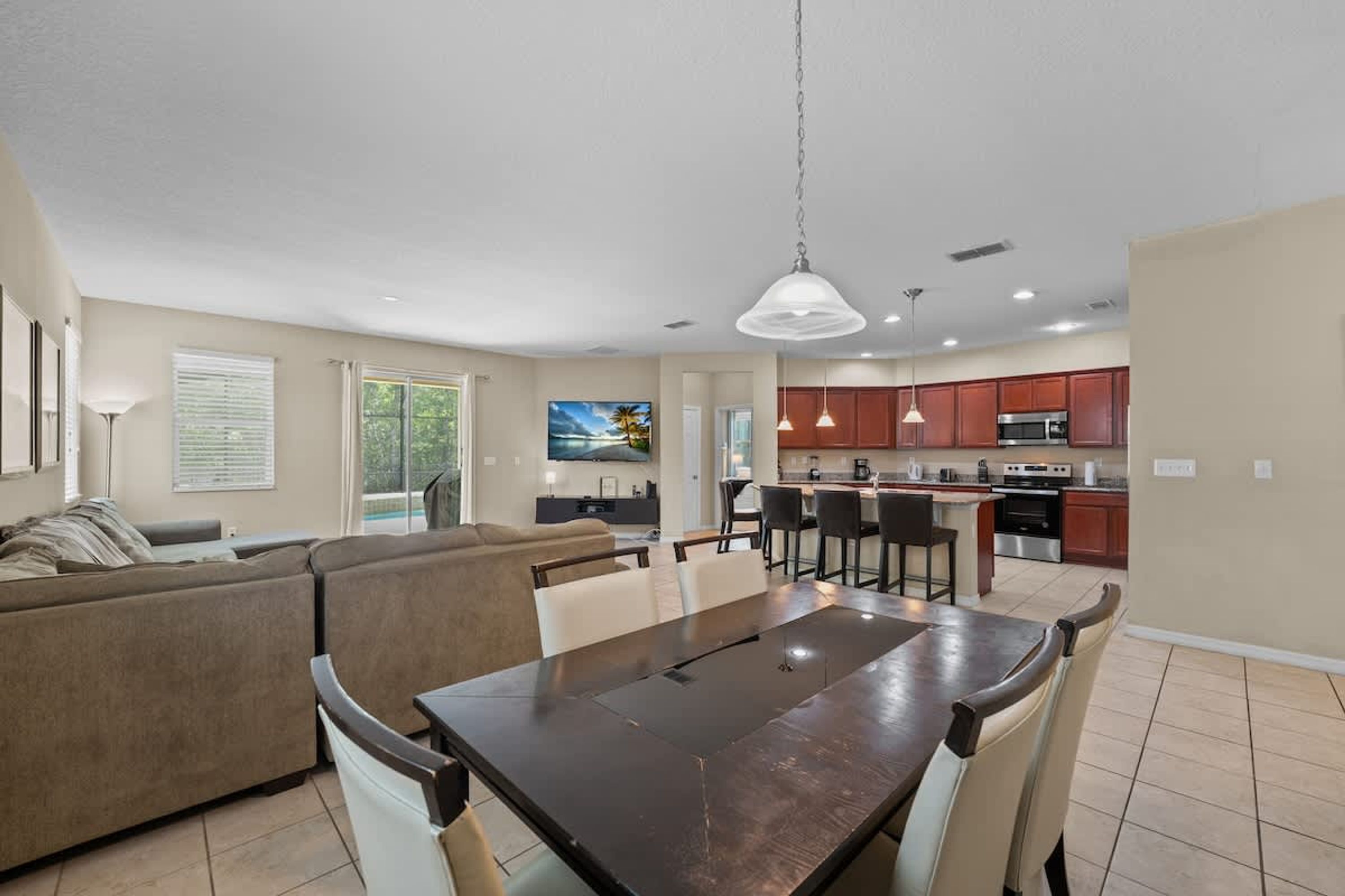 A modern kitchen with dark cabinets, a dining area with a wooden table and chairs, and a living area with a sofa and a TV.