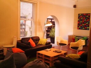 A cozy living room with a sofa, two armchairs, a coffee table, and a bookshelf. - Six Degrees Boutique Hotel (Albany)