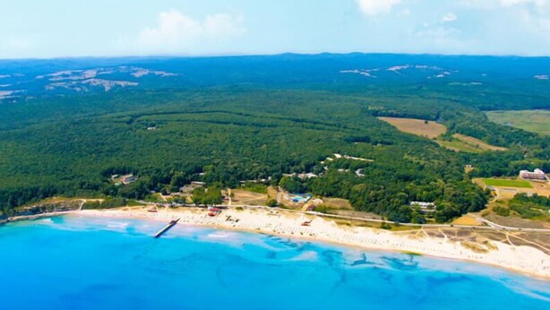 An aerial view of a coastal area with a beach, forested hills, and scattered buildings. - Forest Beach Hotel (Kiten)
